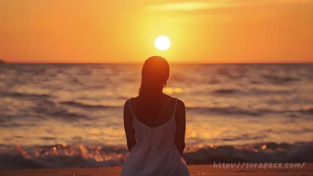 海の夕日を眺める女性